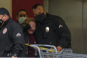 A police officer comforts a woman at the scene where two people were struck by gunfire in a shooting at a Burlington store as part of a chain formerly known as Burlington Coat Factory in North Hollywood, Calif., Thursday, Dec. 23, 2021