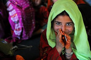 A young Afghan girl smiles shyly after being given a lollipop by an Afghan Local Policeman during a break from her lessons at the Camp 3 school in the internally displaced persons village in Task Force Spartan’s area of operations Nov. 17