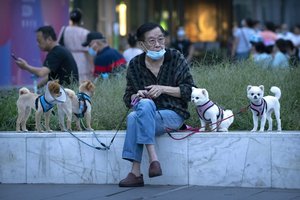 A man wearing a face mask to protect against COVID-19 sits with dogs on leashes near a neighborhood with a suspected coronavirus case in Beijing, Wednesday, Sept. 15, 2021