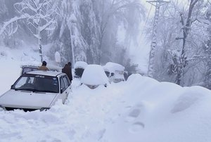 In this photo provided by the Inter Services Public Relations, people walk past vehicles trapped in a heavy snowfall-hit area in Murree, some 28 miles (45 kilometers) north of the capital of Islamabad, Pakistan, Saturday, Jan. 8, 2022