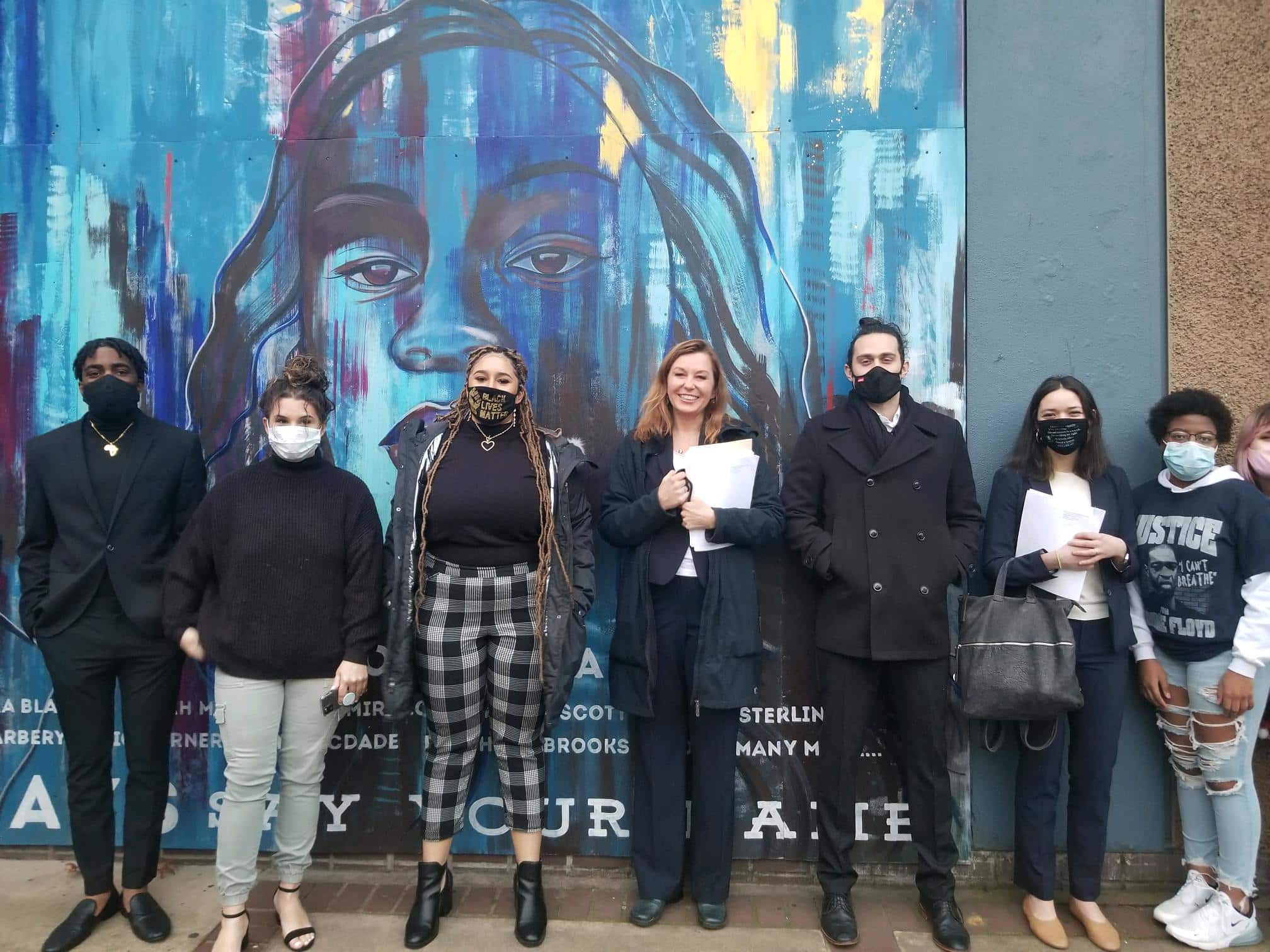 Black Unity members and CLDC lawyers stand in front of a blue and multicolored mural.