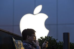 File - A man uses his mobile phone near a Apple store logo in Beijing, China, Friday, May 13, 2016.