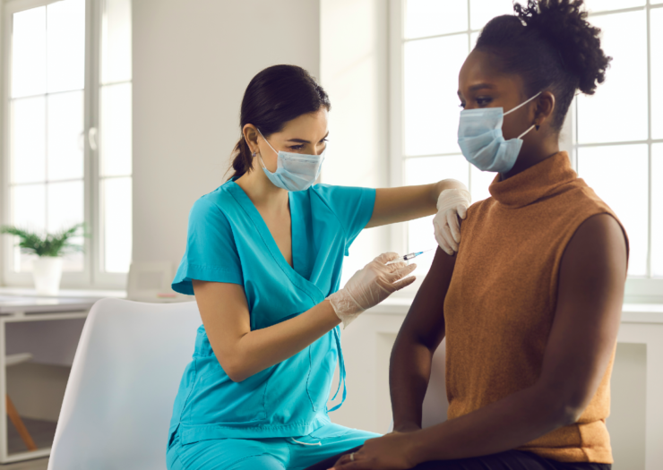 [PHOTO: Young Black woman receives vaccine shot by a health-care worker]