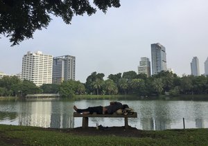 A man sleeps on a bench in front of a lake in Lumphini Park in Bangkok, Thailand, Thursday, Oct. 13, 2016.