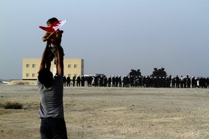 File - A Bahraini anti-government protester holds up a child carrying a national flag toward riot police, Friday, June 15, 2012, in Karbabad, Bahrain, just west of the capital of Manama.