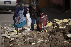 Women help each other walk over the rubble from buildings that fell during the earthquake in San Pedro, Guatemala, Monday, Nov. 12 2012.