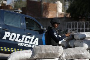 In this Feb. 12, 2020 photo, police stand guard behind a parapet of sandbags, at the entrance to Santa Rosa de Lima, birthplace of a local cartel that goes by the same name, in Guanajuato state, Mexico.