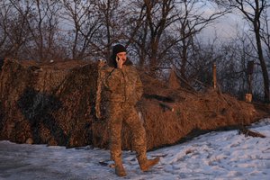 A Ukrainian serviceman is illuminated by the setting sun while talking on the phone at a frontline position outside Popasna, the Luhansk region, in eastern Ukraine, Wednesday, Feb. 16, 2022