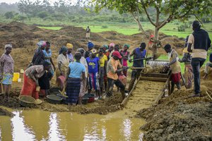 Ugandans process mud they hope contains gold through a sieve at an open-cast gold mining site at which adults and youth work in the village of Mawero, on the outskirts of Busia town, in eastern Uganda Monday, Oct. 18, 2021.