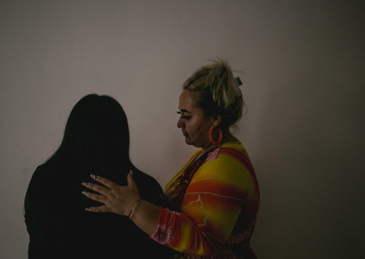 [Photo: A young woman stands with her back to the camera, her mother next to her with one hand on her shoulders.]