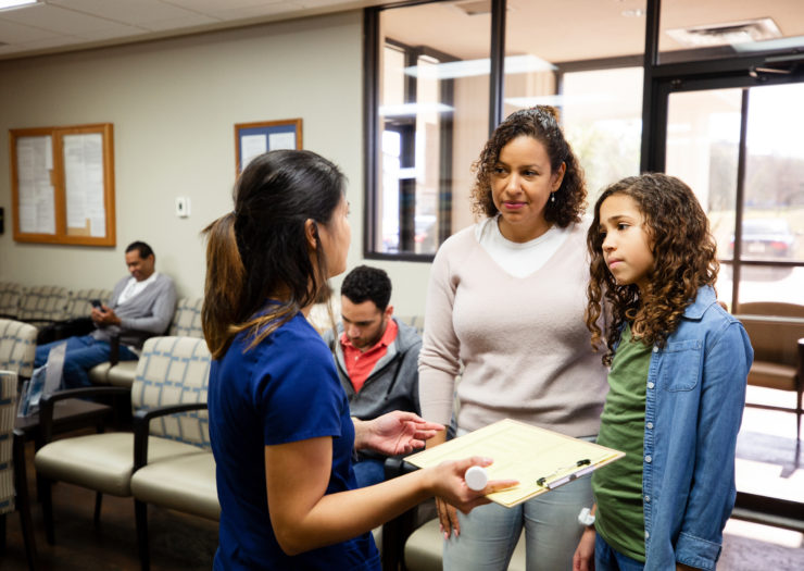 Photo of mother and young teen daughter at the doctor's office talking to a nurse