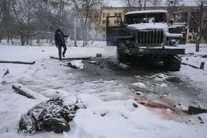 The body of a serviceman is coated in snow as a man takes photos of a destroyed Russian military multiple rocket launcher vehicle on the outskirts of Kharkiv, Ukraine, Feb. 25, 2022