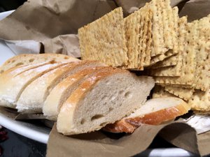 Wheat crackers, and sliced bread load on a platter, served at a restaurant. Taken on July 2017.