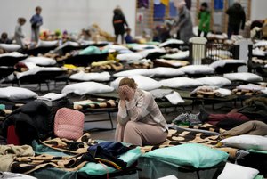 A woman puts her head in her hands as she sits on a cot in a shelter, set up for displaced persons fleeing Ukraine, inside a school gymnasium in Przemysl, Poland, Tuesday, March 8, 2022. U.N. officials said Tuesday that the Russian onslaught has forced more than 2 million people to flee Ukraine.