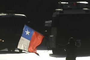 An anti-government protester waves a Chilean flag before police vehicles parked in Italy Plaza in Santiago, Chile, Friday, Dec. 17, 2021.