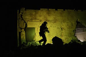 A Ukrainian special police officer walks next to a destroyed building as he patrols during night curfew in Kharkiv, Ukraine, Sunday, March 27, 2022.