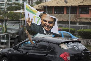 A supporter waves a flag with an image of Jair Bolsonaro as he drives past in front of his residence in Rio de Janeiro, Brazil, Monday, Oct. 29, 2018.