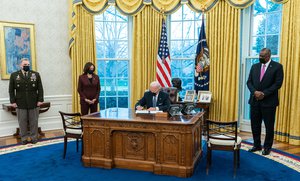 President Joe Biden, joined by Vice President Kamala Harris, Secretary of Defense Lloyd Austin (right) and Chairman of the Joint Chiefs Mark Milley (left), signs an executive order rescinding a band on transgender individuals serving in the military Monday, Jan. 25, 2021, in the Oval Office of the White House