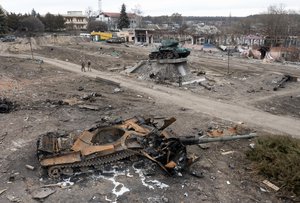 Local residents pass at a damaged Russian tank in the town of Trostsyanets, some 400km (250 miles) east of capital Kyiv, Ukraine, Monday, March 28, 2022. The monument to Second World War is seen in background.