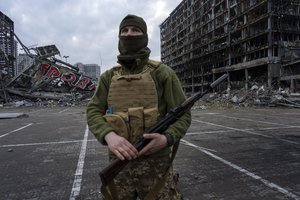 A soldier poses for the picture in Kyiv, Ukraine, Wednesday, March 30, 2022, while standing guard amid the destruction caused after shelling of a shopping center on March 21