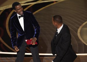 Presenter Chris Rock, left, reacts after being hit on stage by Will Smith while presenting the award for best documentary feature at the Oscars on Sunday, March 27, 2022, at the Dolby Theatre in Los Angeles