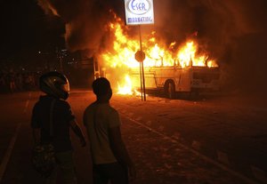 Sri Lankans watch after setting a bus on fire during a protest outside Sri Lankan president's private residence on the outskirts of Colombo, Sri Lanka, Friday, April 1, 2022.