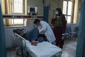 A doctors looks after a patient as a Taliban stands behind him in Wazir Mohammad Akbar Khan National Hospital, in Kabul Afghanistan, on Monday, Dec. 5, 2021