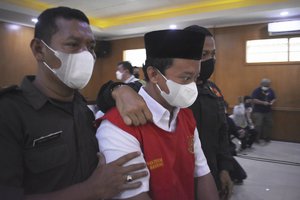 Security officers escort Herry Wirawan, center, the principal of a girls-only Islamic boarding school who is accused of raping his students, during his sentencing hearing at a district court in Bandung, West java, Indonesia, Tuesday, Feb. 15, 2022