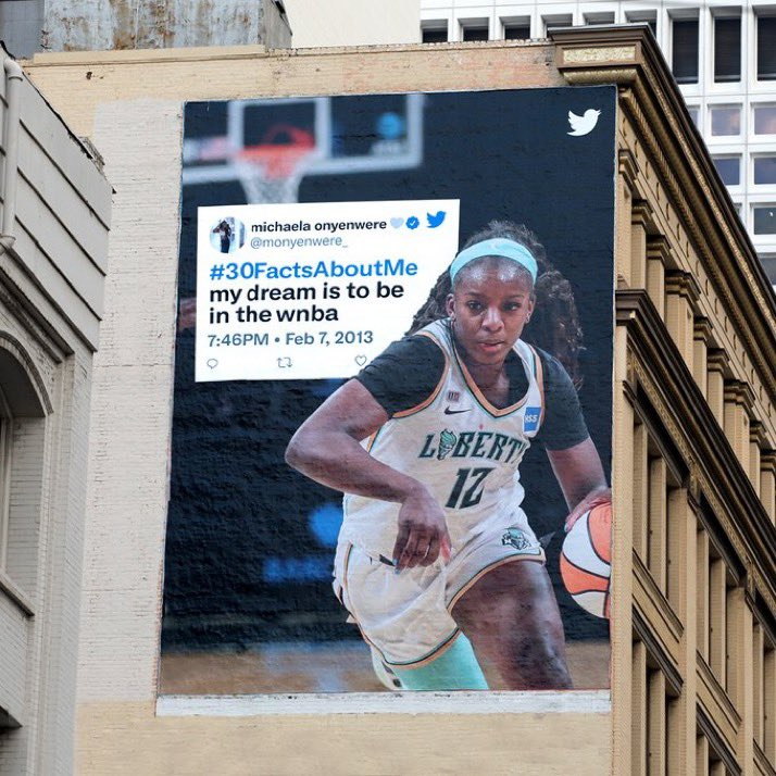 Image of a billboard in San Francisco of a Tweet from Michaela Onyenwere that reads "#30FactsAboutMe my dream is to be in the wnba" from February 2013. The Tweet is overlaid on an image of her  playing in the WNBA. 