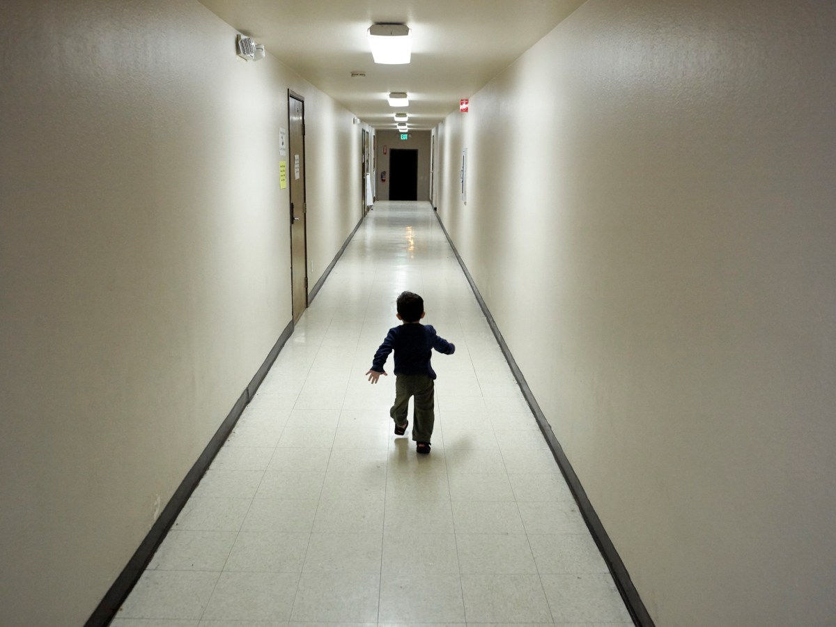 A small boy runs down a long empty hallway on his own.