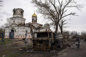 A woman with a bicycle rides by a burned vehicle, in front of a damaged Church in Lukashivka, near the city of Chernihiv in northern Ukraine, on Friday, April 22, 2022.