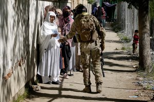 A Taliban fighter stands guard as people line up to enter the government passport office, in Kabul, Afghanistan, Wednesday, April 27, 2022.