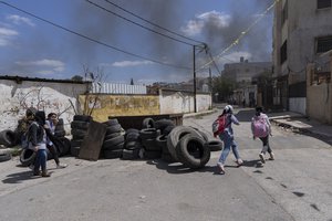 Palestinian students walk past piles of tires that are collected and prepared to be set on fire during possible future Israeli army incursions, in the West Bank refugee camp of Jenin, Tuesday, April 12, 2022.