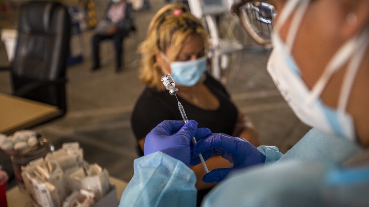 LOS ANGELES, CA - JANUARY 27: (Editor's note: This photo is initially for a Hayley Smith story.) Gabriela Martinez, right, is preparing a vaccination for Blandly Amaya at South Central Family Health Center on Thursday, Jan. 27, 2022 in Los Angeles, CA. The center is located in a neighborhood with the highest Omicron case rates in the county. (Francine Orr / Los Angeles Times)