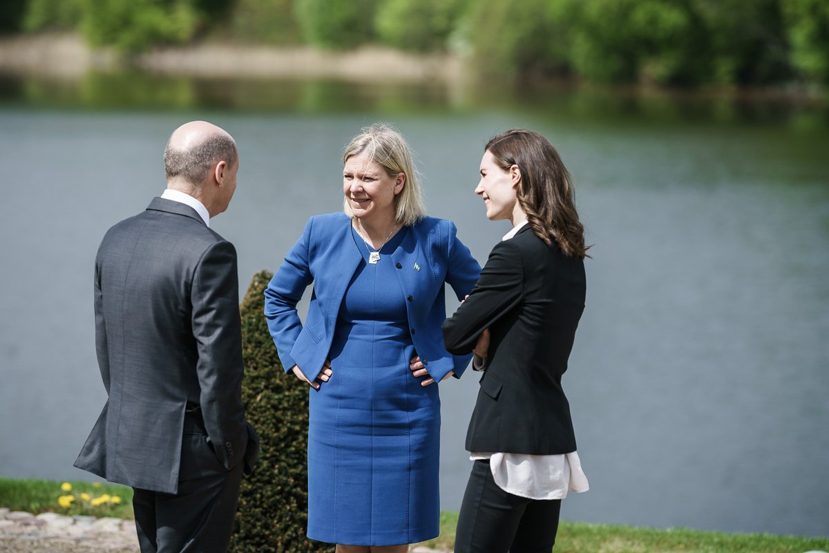 Bundeskanzler Scholz steht der schwedischen Ministerpräsidentin Andersson gegenüber und unterhält sich. Er hat die Hände in den Taschen, Magdalena Andersson trägt ein blaues Kleid. Neben ihr steht die finnische Ministerpräsidentin Sanna Marin. Im Hintergrund ist ein See zu sehen.