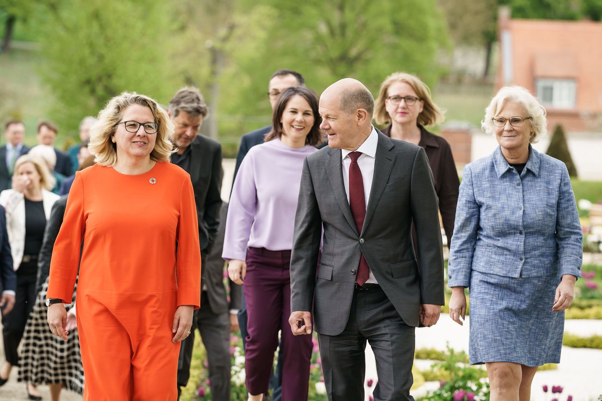 Bundeskanzler Scholz läuft mit einem Teil des Kabinetts über einen Weg im Schloss Meseberg. Neben ihm sind die Ministerinnen Lambrecht und Schulze zu erkennen. Hinter dem Kanzler lacht Außenministerin Baerbock , neben ihr läuft Ministerin Paus.