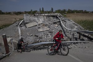 Teenagers on bicycles pass a bridge destroyed by shelling near Orihiv, Ukraine, Thursday, May 5, 2022.