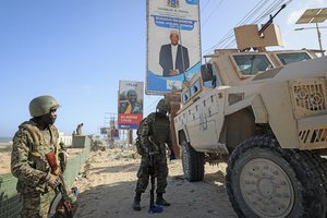 Ugandan peacekeepers with the African Transition Mission in Somalia (ATMIS) stand next to their armored vehicle, with a campaign poster for presidential candidate Ahmed Abdullahi Samow seen above, on a street in Mogadishu, Somalia Tuesday, May 10, 2022.