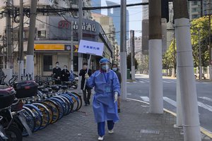 A worker in protective gear holds a sign which reads "Do not crowd" during a mass testing day for residents in a lockdown area in the Jingan district of western Shanghai Monday, April 4, 2022