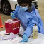 A nurse in blue PPE preparing vaccines.