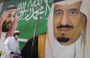 A man walks past a banner showing Saudi King Salman, right, and his son Crown Prince Mohammed bin Salman, outside a mall in Jiddah, Saudi Arabia