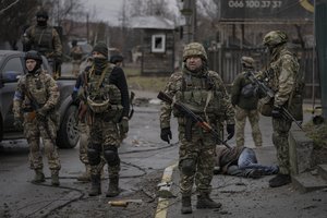 Ukrainian servicemen stand while checking bodies of civilians for booby traps, in the formerly Russian-occupied Kyiv suburb of Bucha, Ukraine, Saturday, April 2, 2022