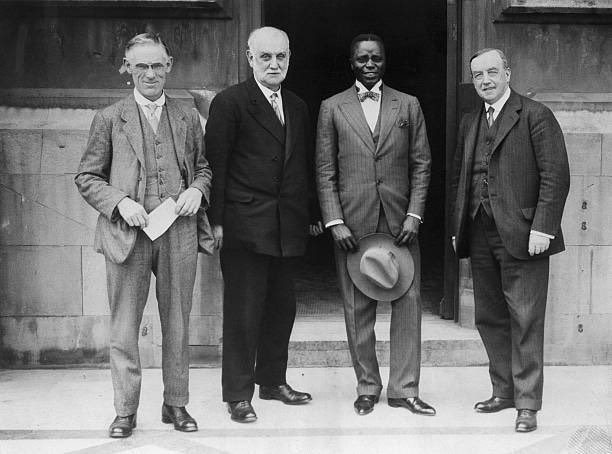 Clements Kadalie in London, England on 15 July 1927. He has two men to his right and one to his left. All four are dressed in suits and Clements is holding his hat a little below his waist.