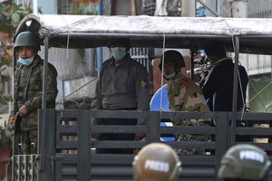 A man aims a rifle from inside a vehicle while a soldier holds a slingshot during a crackdown on anti-coup protesters holding a rally in front of the Myanmar Economic Bank in Mandalay, Myanmar on Monday, Feb. 15, 2021