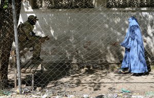 A Taliban fighter stands guard as a woman enters the government passport office, in Kabul, Afghanistan, Wednesday, April 27, 2022.