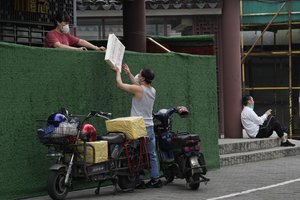 A man pass materials to a woman across a barrier built around a community, Thursday, June 2, 2022, in Shanghai