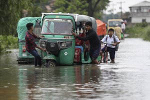 People push an auto rickshaw through a flooded road as a school boy rides his bicycle behind in Bagha area in Sylhet, Bangladesh, Monday, May 23, 2022.