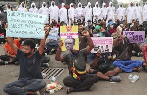 Supporters of the independence of the West Papua hold posters as police officers in protective suits look on during a rally commemorating the 60th anniversary of the failed efforts by Papuan tribal chiefs to declare independence from Dutch colonial rule in 1961, in Jakarta