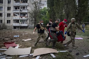 Paramedics carry the body of a woman who was killed during a Russian bombardment at a residential neighborhood in Kharkiv, Ukraine, on Thursday, July 7, 2022