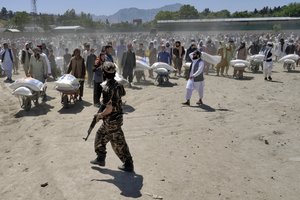 File - A Taliban fighter stands guard as people receive food rations distributed by a Chinese humanitarian aid group, in Kabul, Afghanistan, Saturday, April 30, 2022. Afghanistan expects that 1.1 million children under the age of 5 will face malnutrition in the country by the end of this year, as hospitals wards are packed with sick children from sever hunger and malnutrition.